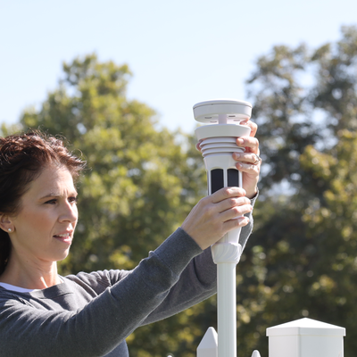 woman mounting the Tempest weather station on a pole in the garden