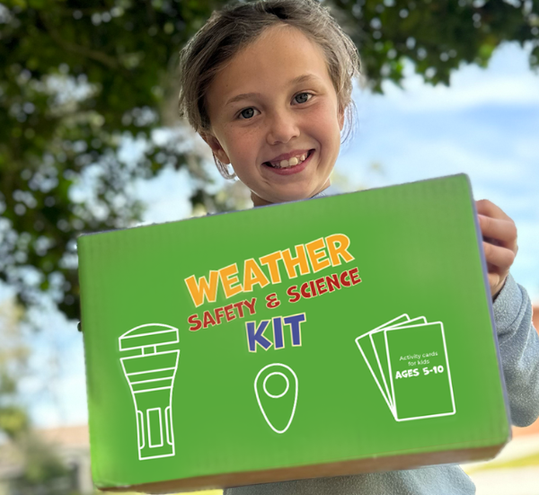 A young girl smiling and holding a green Weather Safety & Science Kit box