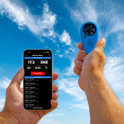 A hand holding the Tempest WEATHERmeter in the sky with another hand holding a smartphone with Tempest app